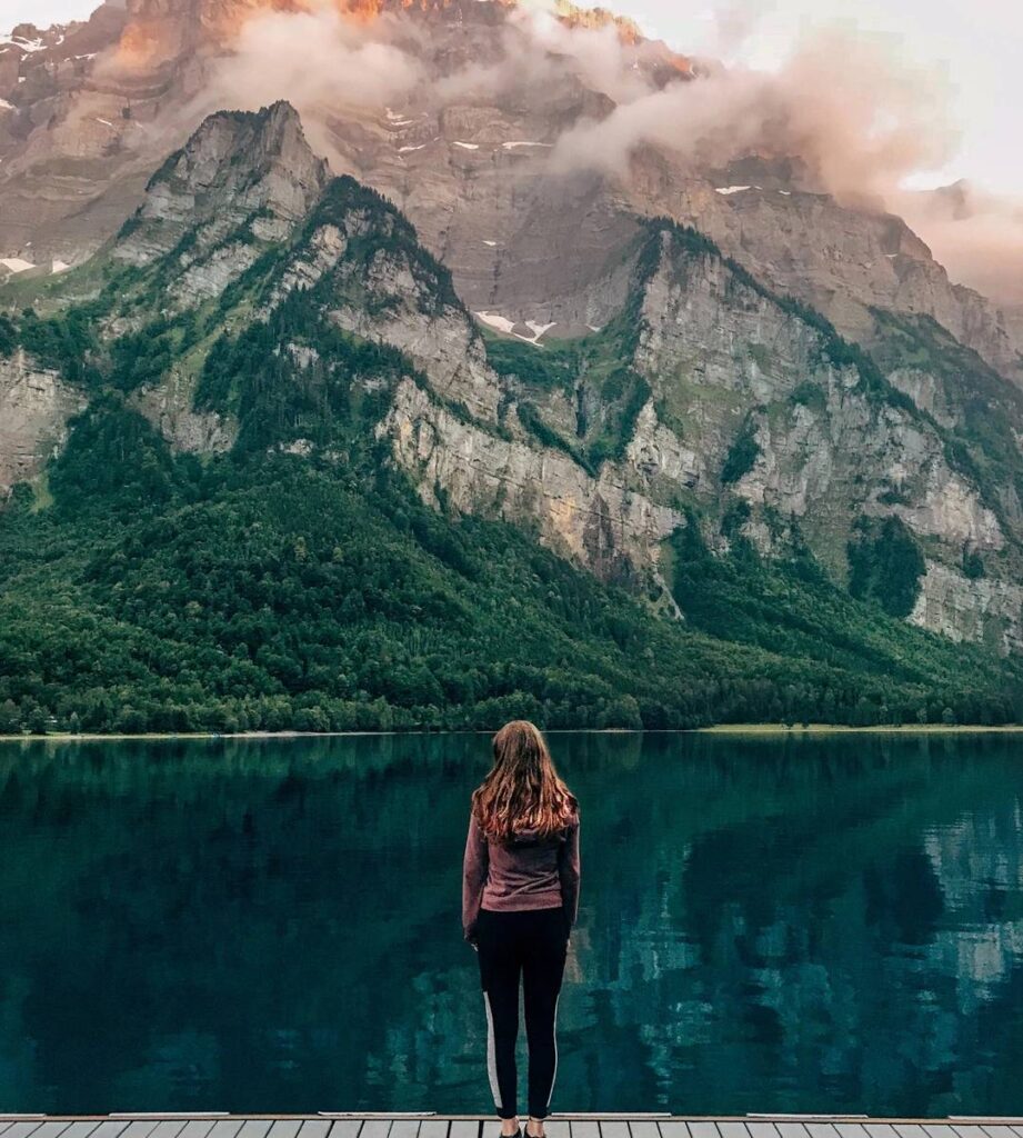 Woman standing serenely before beautiful view of alpine lake and scenic mountain view