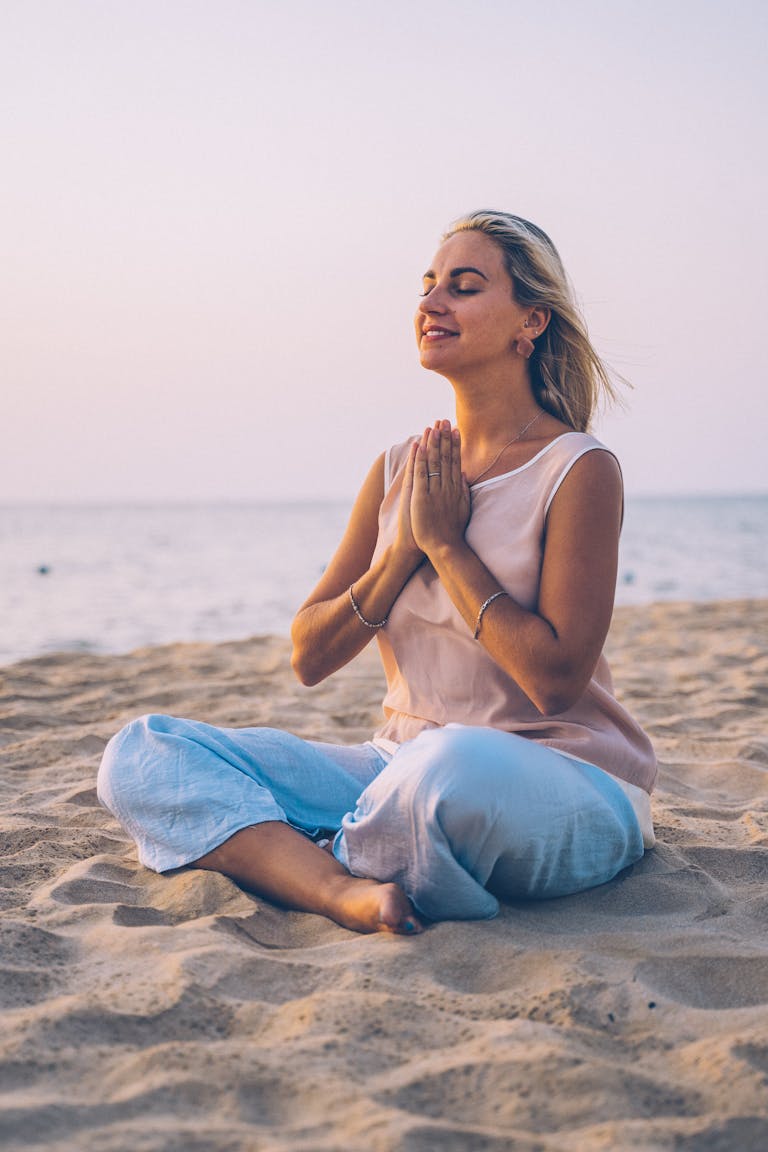 Adult woman practicing meditation on a serene beach during sunset, exemplifying relaxation and mindfulness.