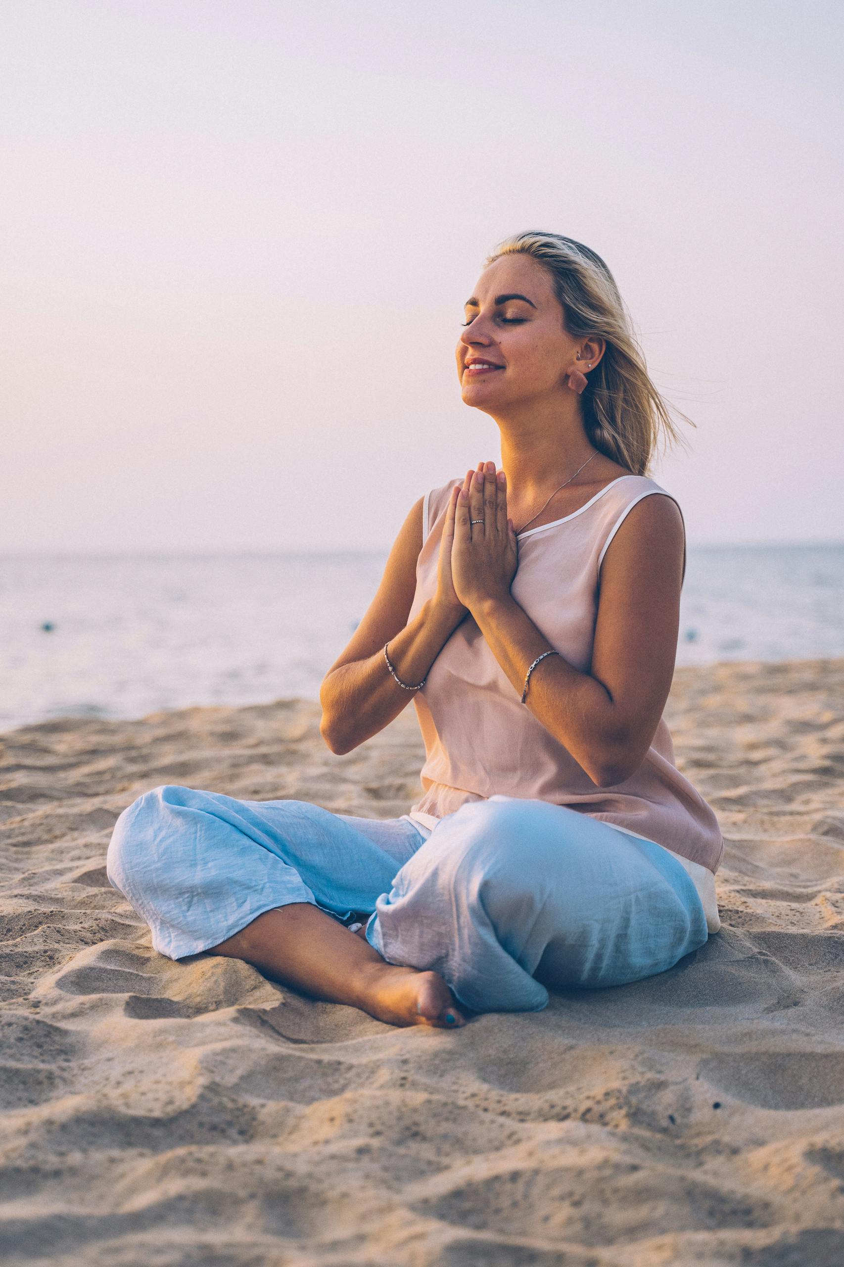 Adult woman practicing meditation on a serene beach during sunset, exemplifying relaxation and mindfulness.