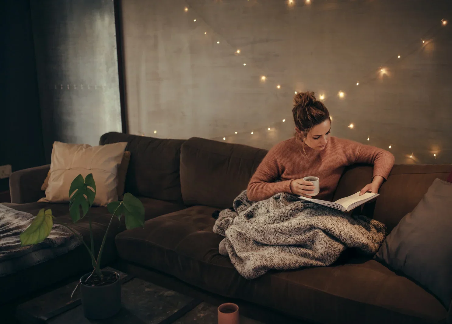 Woman winding down in the evening with a book instead of a screen, and tea instead of alcohol