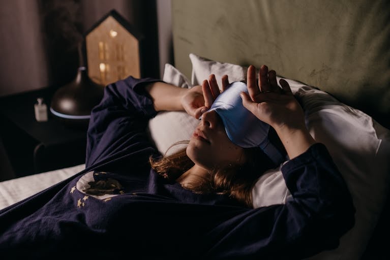 A woman in perimenopause rests indoors wearing a sleep mask, sleeping lightly
