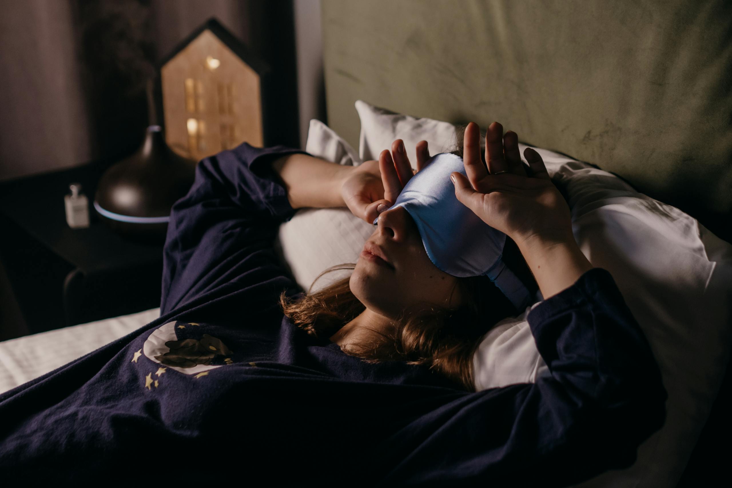 A woman in perimenopause rests indoors wearing a sleep mask, sleeping lightly