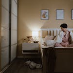 Asian woman in perimenopause, wearing pajamas sitting on bed, unable to sleep