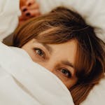 Cozy close-up of a woman with manicured nails peeking out from a white sheet.