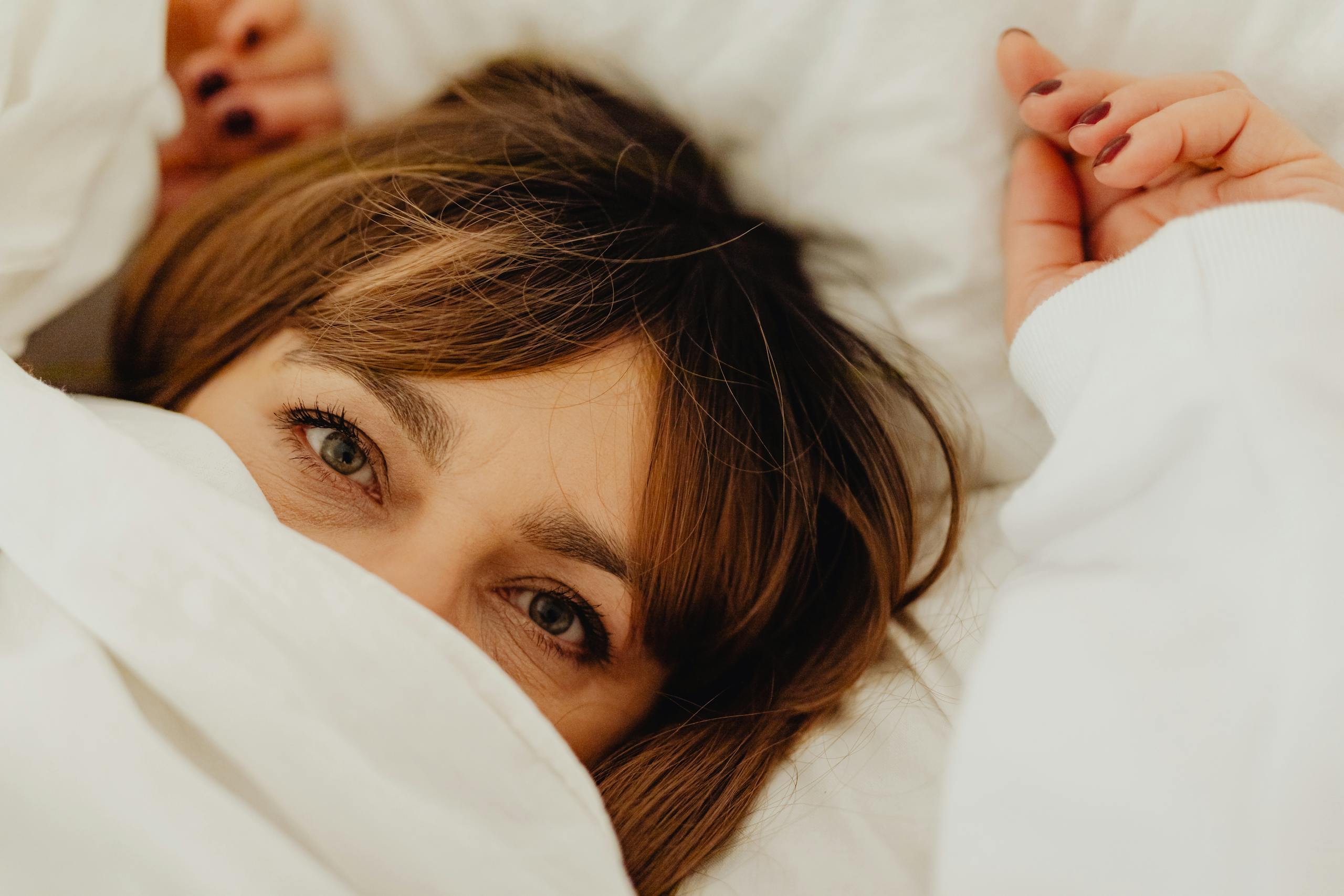 Cozy close-up of a woman with manicured nails peeking out from a white sheet.