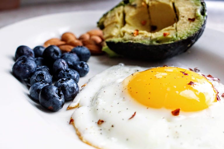 A nutritious breakfast featuring a fried egg, avocado, blueberries, and almonds - a great combination of protein and fiber.