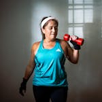 Middle-aged, perimenopausal woman in workout attire lifting a red dumbbell. Indoor exercise scene promoting fitness and healthy lifestyle.