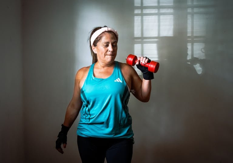Middle-aged, perimenopausal woman in workout attire lifting a red dumbbell. Indoor exercise scene promoting fitness and healthy lifestyle.