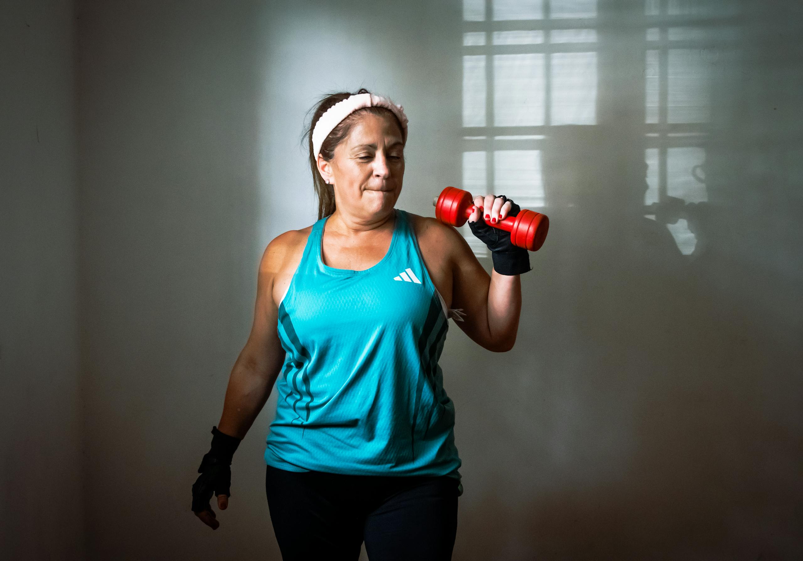 Middle-aged, perimenopausal woman in workout attire lifting a red dumbbell. Indoor exercise scene promoting fitness and healthy lifestyle.