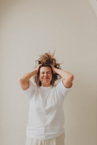 A Caucasian woman with long hair shows frustration as she stands against a white background.