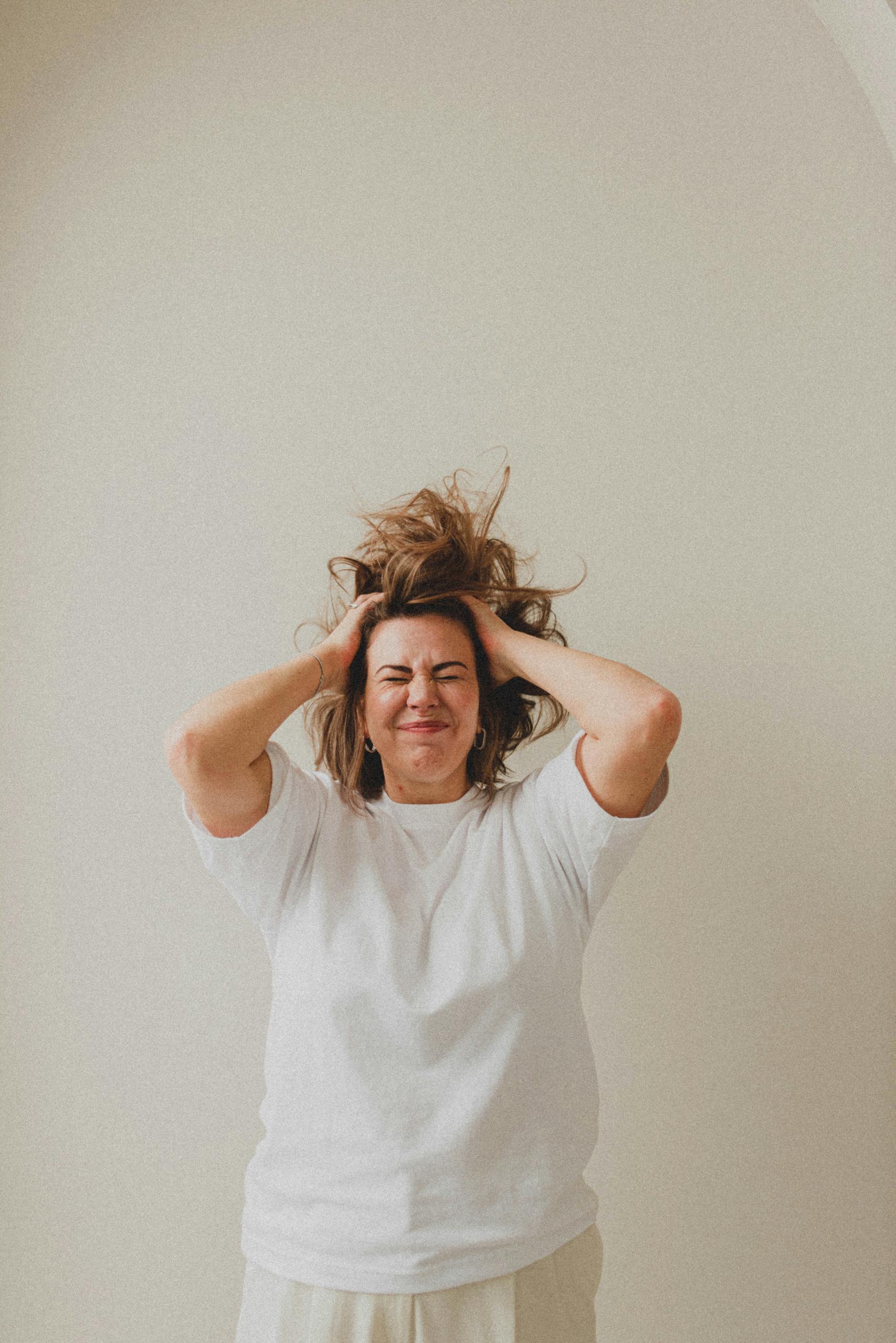 A Caucasian woman with long hair shows frustration as she stands against a white background.