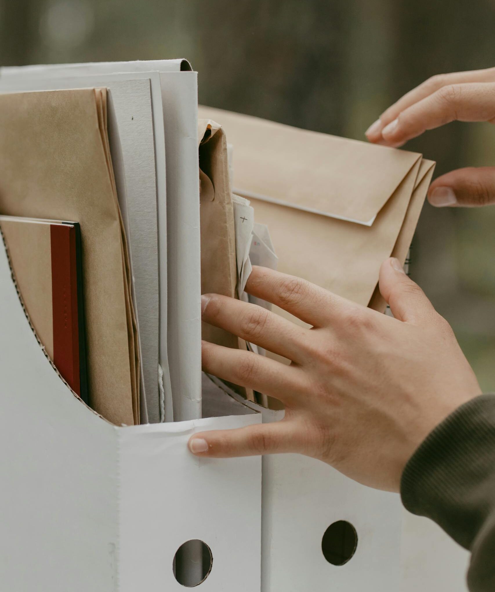 Close-up of hands sorting and organizing documents in a file box outdoors.