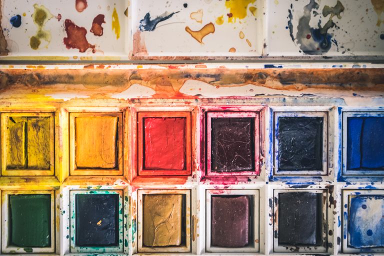 A colorful close-up of a used watercolor paint palette with vibrant hues.